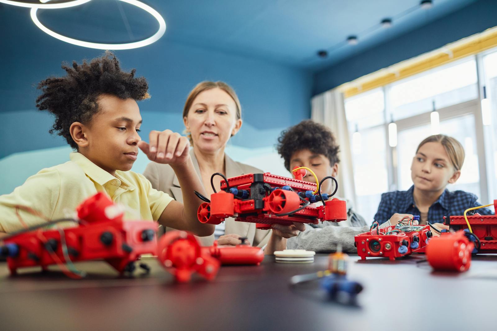 Mokytoja konsultuoja mokinius, dirbančius su robotikos projektu klasėje.